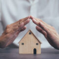 Home security concept, insurance for real estate, protecting gesture of man and house model.
